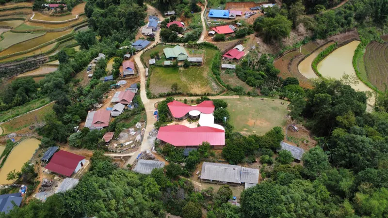 Aerial view of red-roofed school buildings clustered among terraced rice paddies and village homes