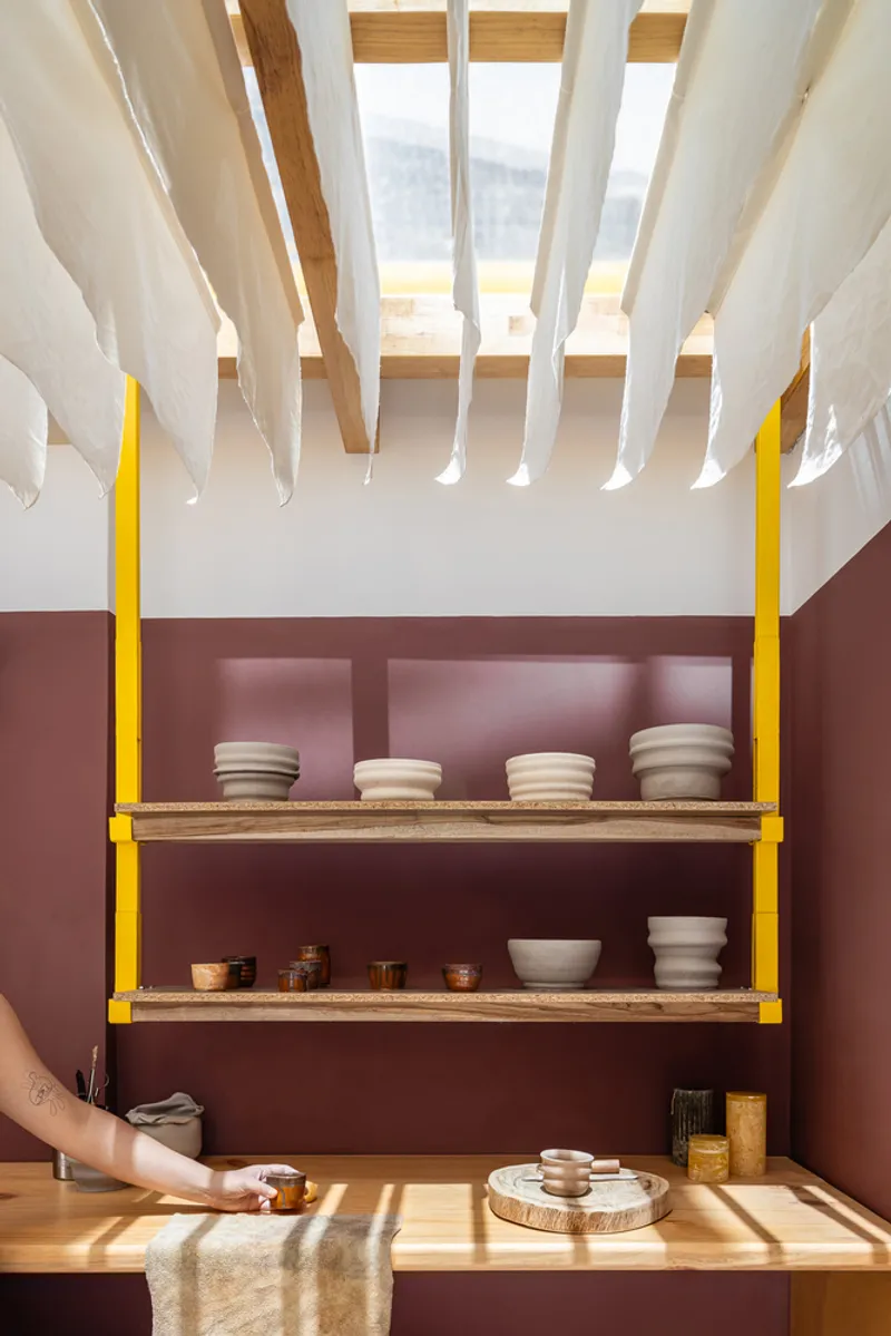 Yellow steel shelving brackets against maroon wall with ceramic vessels in afternoon light
