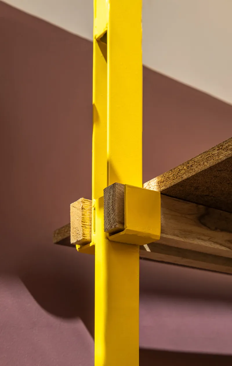 Detail of a yellow painted steel column meeting a raw timber beam in soft daylight