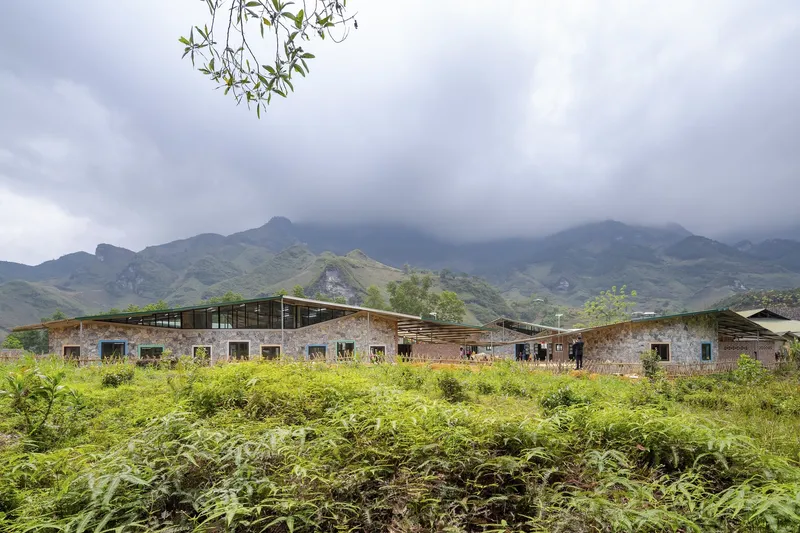 Long stone facade with timber-framed clerestory windows extending across a field of ferns under cloudy skies