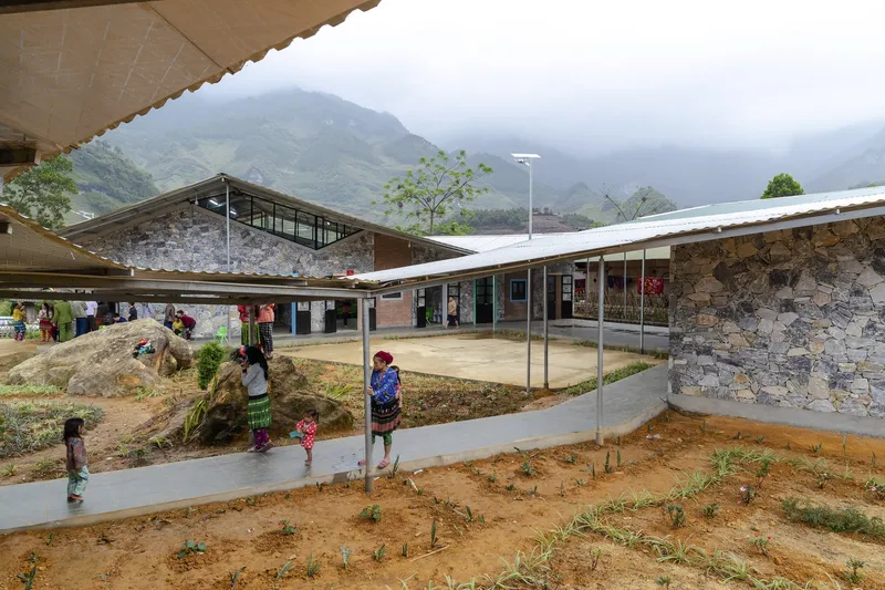 Courtyard with curved concrete paths and a rock formation surrounded by low stone buildings with children walking