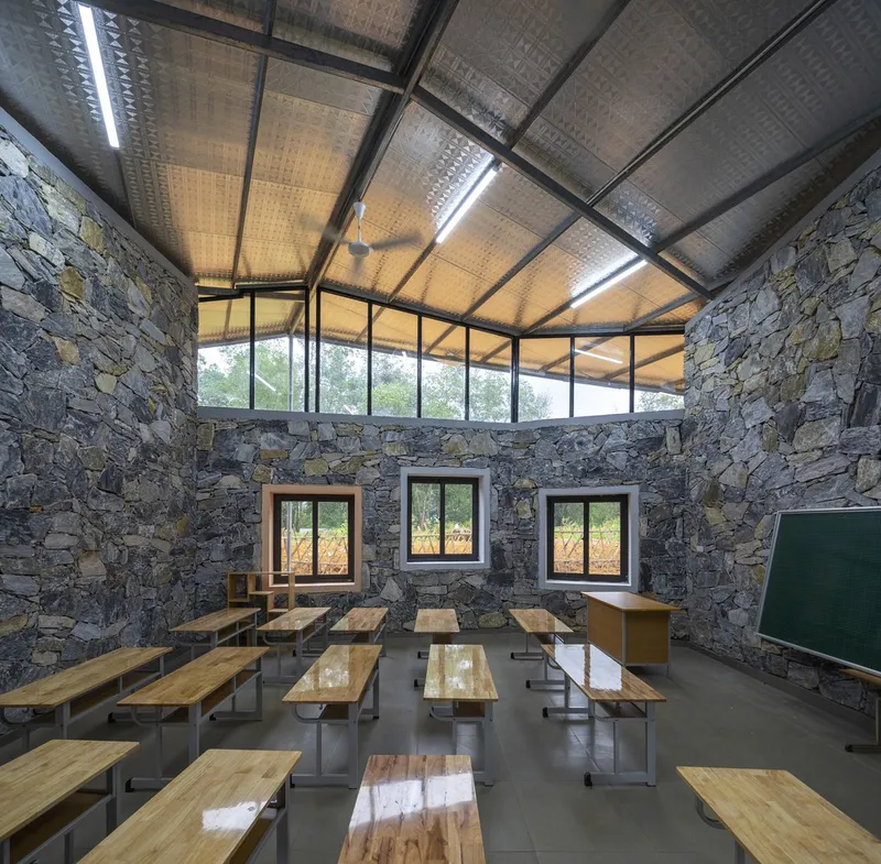 Classroom with timber desks arranged in rows beneath a clerestory window and translucent corrugated ceiling panels