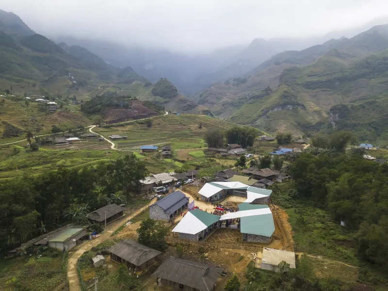 Aerial view of clustered buildings with metal roofs in a mountain valley amid terraced fields