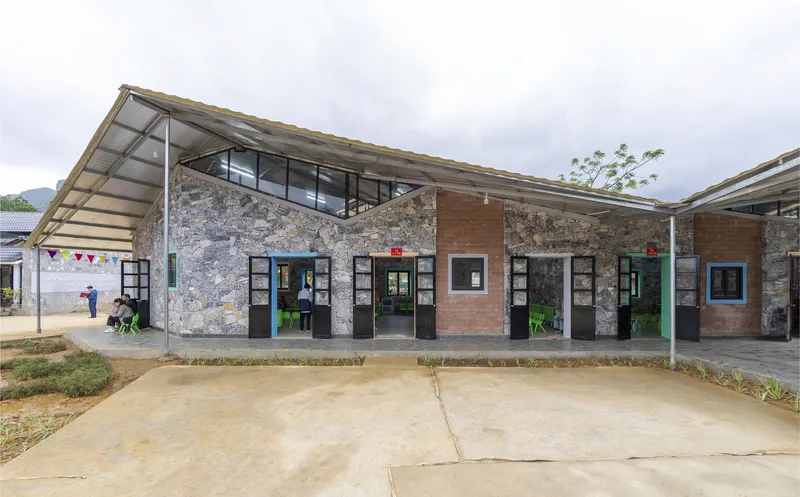 Stone and brick facade with cantilevered metal roof and black-framed doors under an overcast sky
