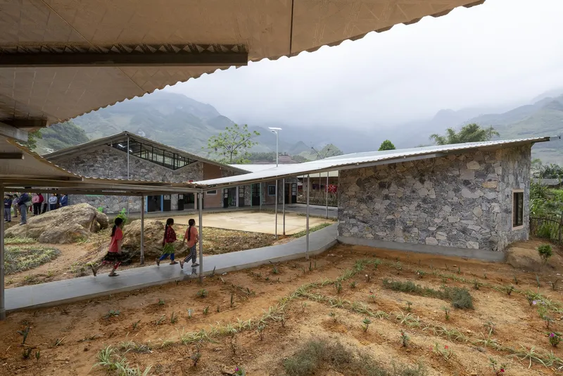 View across courtyard showing stone volumes with overhanging eaves and planted beds with misty mountains beyond