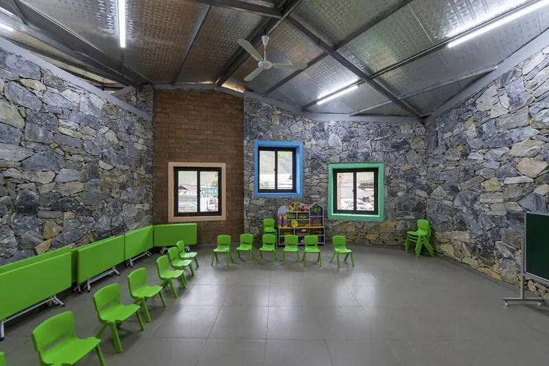 Classroom interior with stone walls, green plastic chairs, and a corrugated metal roof with exposed steel beams