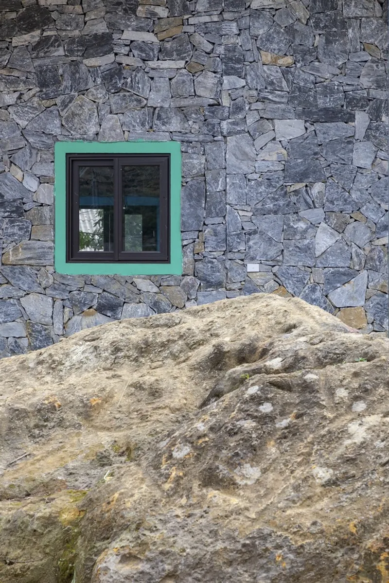 Green-framed window set into irregular grey stone wall above a weathered boulder outcrop