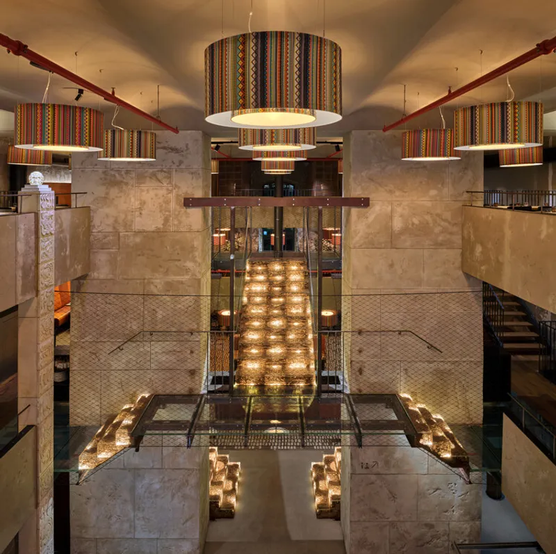 Overhead view of a multi-level restaurant interior with travertine walls and striped textile pendant fixtures