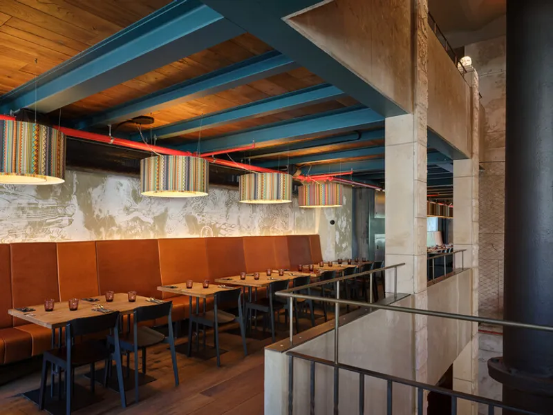 Banquette seating row along a concrete wall beneath timber joists with red conduit piping