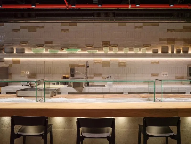 Kitchen counter with glass sneeze guards below a tiled wall with integrated strip lighting