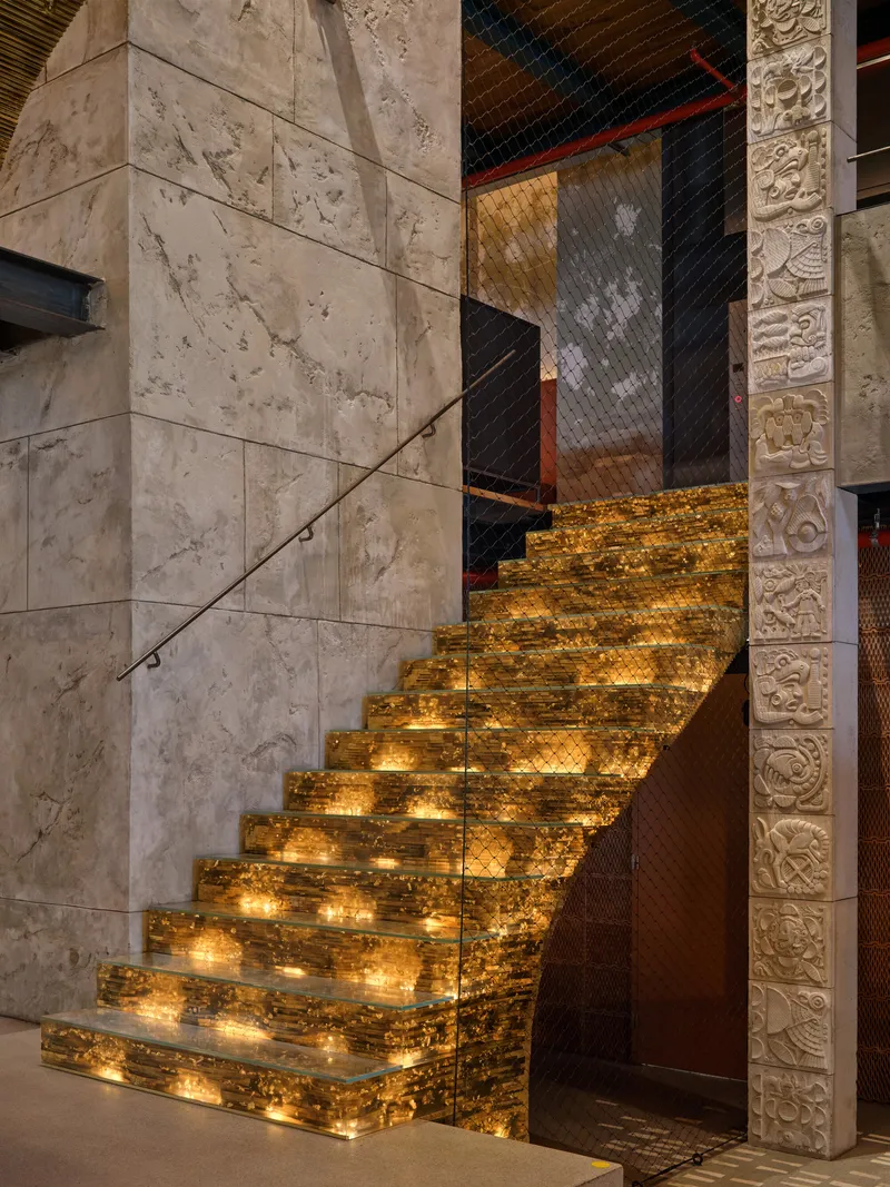 Illuminated staircase with backlit amber resin treads flanked by travertine walls and carved stone