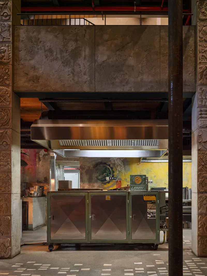 Open kitchen with stainless steel hood and equipment framed by travertine panels and carved columns