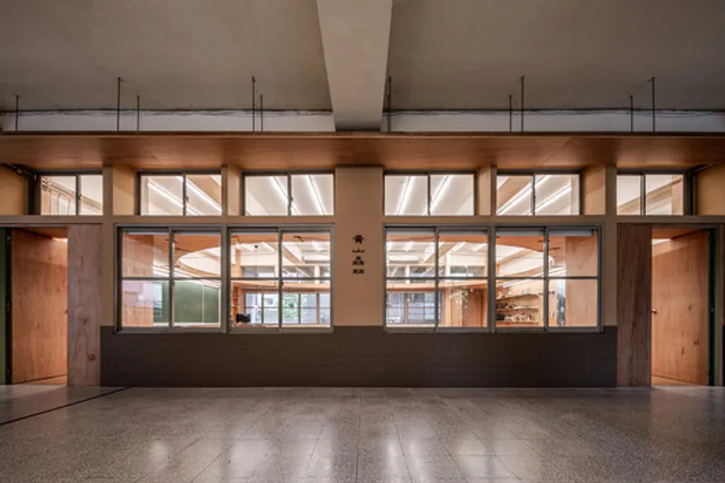 Timber-framed glazed partition with reception desk beneath a concrete soffit at dusk