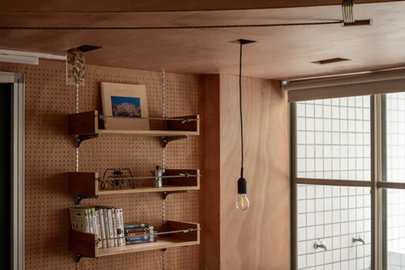 Pegboard wall with floating shelves and pendant bulb beside a translucent glass block window