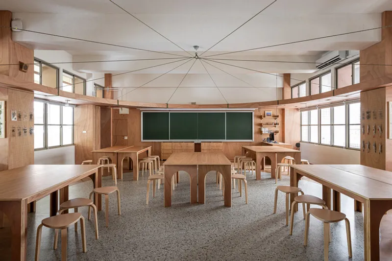 Classroom interior with radial ceiling cables, timber furniture and chalkboard between windows