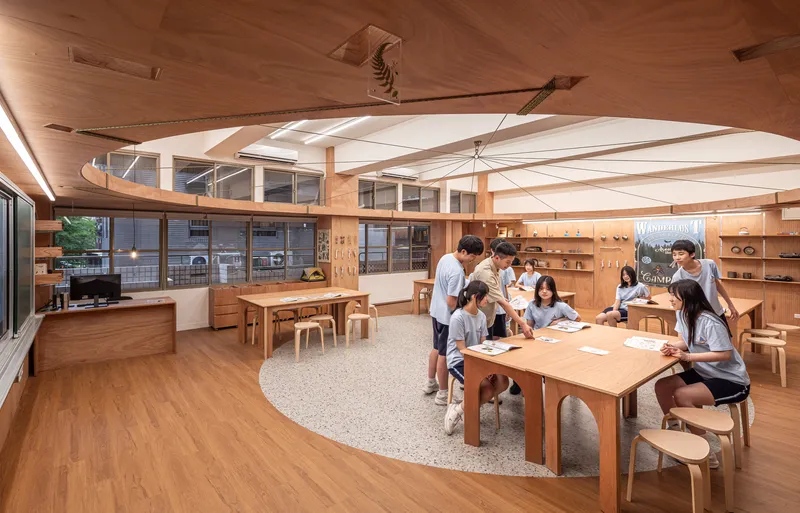 Students gathered around work tables in the timber-lined classroom with terrazzo flooring and afternoon sunlight