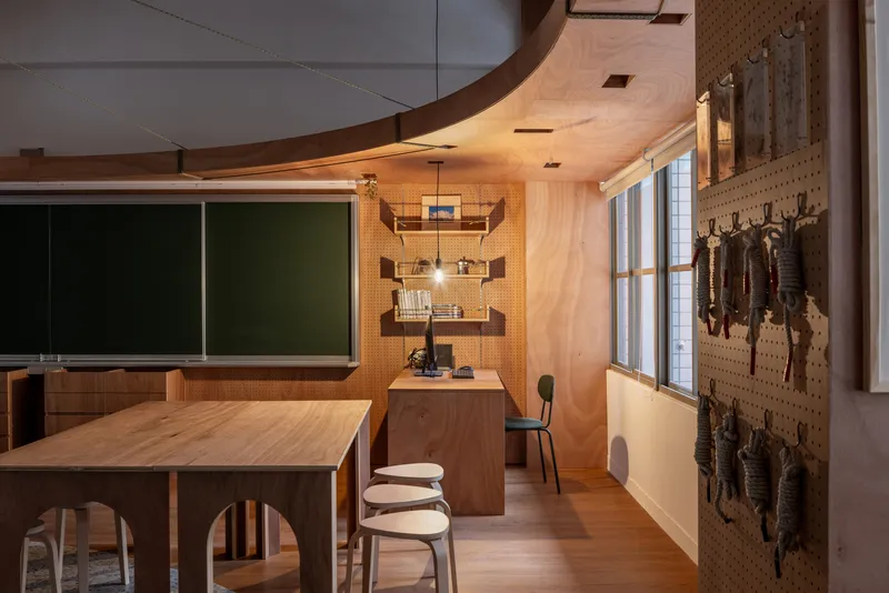 Workshop classroom interior with plywood ceiling, pegboard tool wall, timber tables and green chalkboards