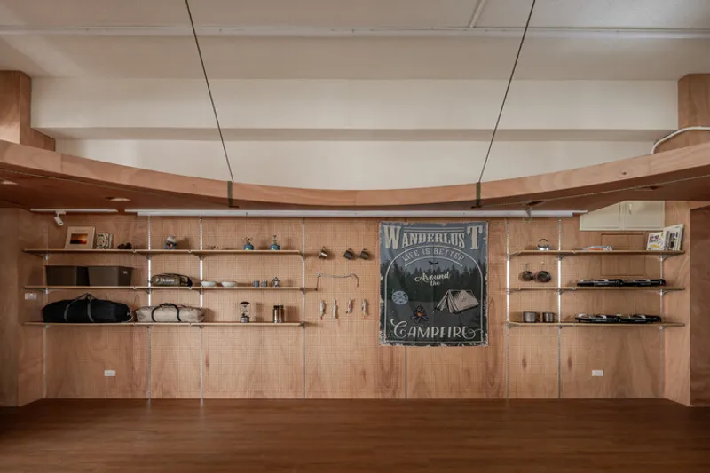 Plywood pegboard storage wall with curved timber beams, open shelving and camping poster centerpiece