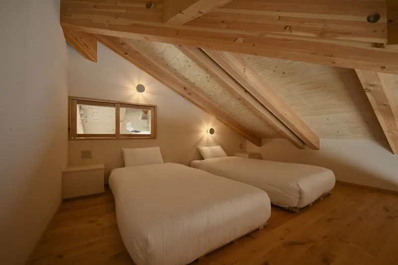 Attic bedroom with sloped timber ceiling, two beds and small transom windows