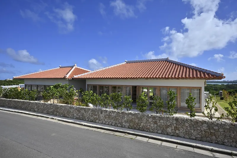 Street view of the terracotta tile roof residence behind a stone masonry wall under white clouds