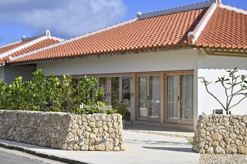 Street view of a low-slung residence with orange tile roof and coral stone perimeter walls
