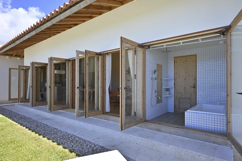 Folding timber-framed glass doors opening bathroom with white mosaic tile to a lawn courtyard