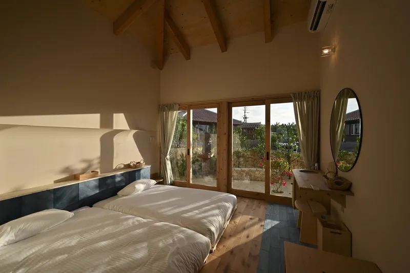 Bedroom interior with timber-framed doors opening to a courtyard under afternoon sunlight