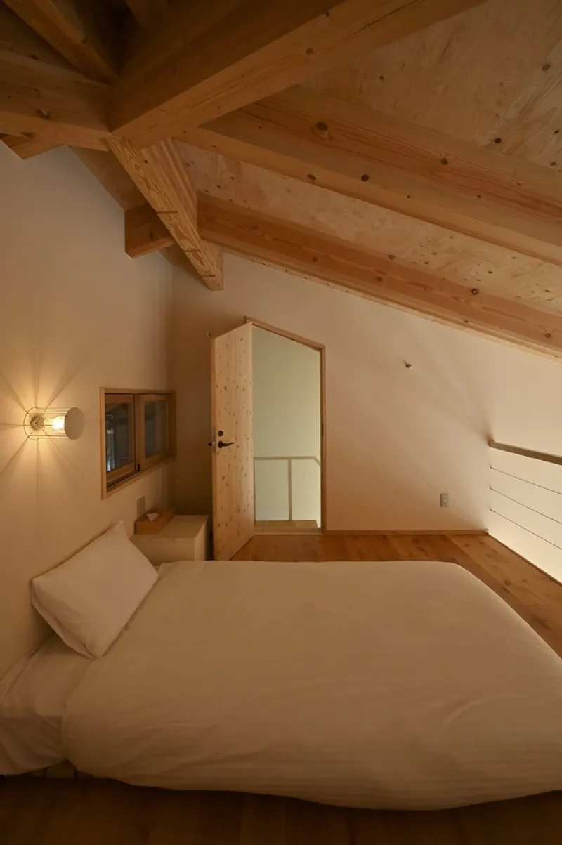 Bedroom with exposed timber ceiling beams and a wall sconce casting light at dusk
