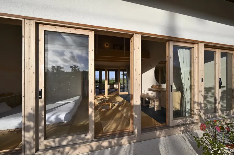 Row of timber-framed glass doors opening from a bedroom to a covered terrace in afternoon light