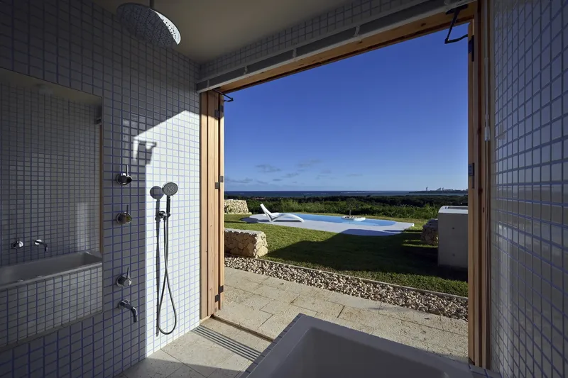 White tiled bathroom with timber-framed door opening directly onto a lawn and swimming pool
