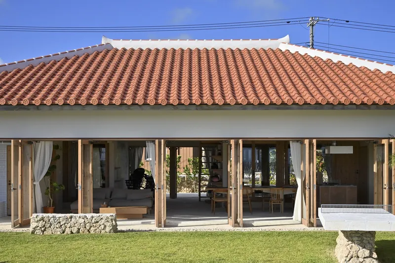 Terracotta tile roof overhanging a row of timber-framed glass doors facing a lawn