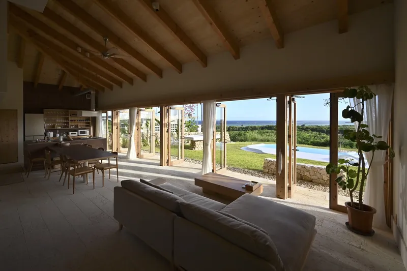 Open living and dining space with exposed timber beams and full-height glazing overlooking a pool