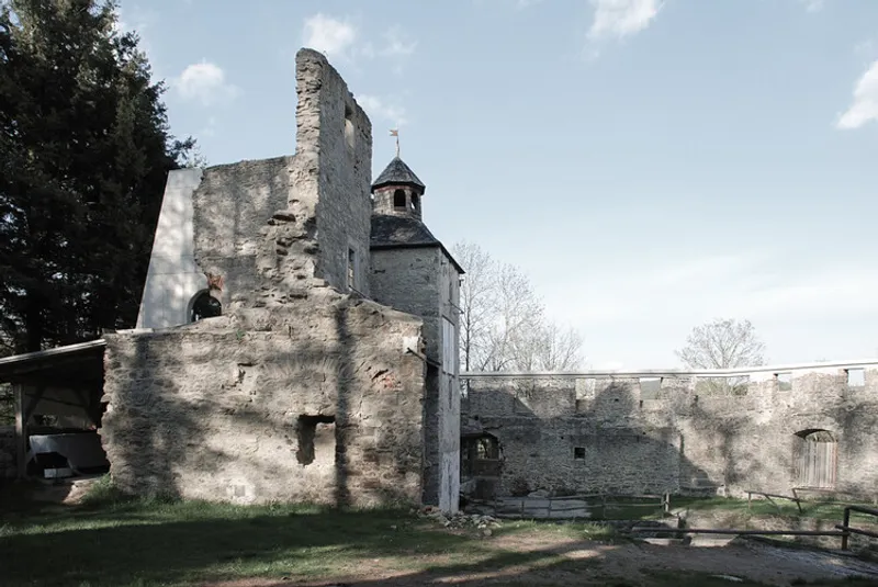 Weathered stone ruins with arched openings and bell tower rising behind fortified walls in spring