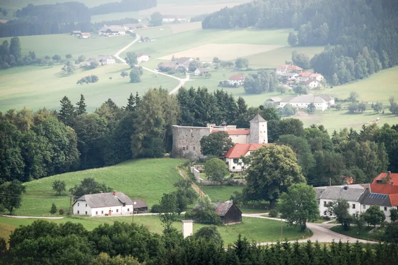 Hilltop castle complex with stone walls and red tile roofs overlooking a valley hamlet below