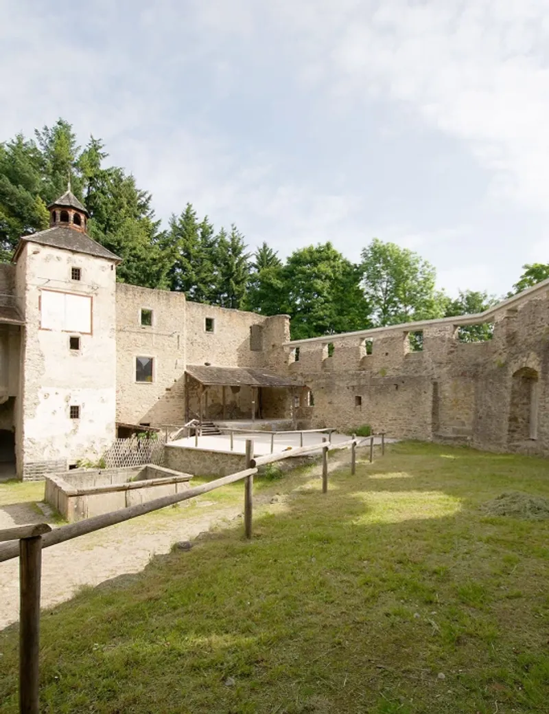 Grassy inner courtyard surrounded by stone battlements and tower with timber shelter in the center