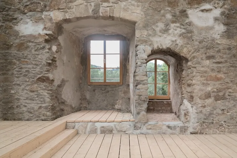 Interior view of two arched window openings in rough stone walls with new timber flooring below