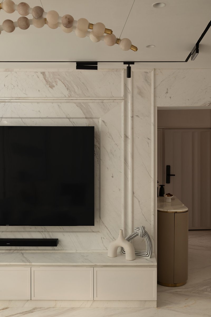 The media wall, with a carved marble frame and a curved fluted side cabinet in brass.