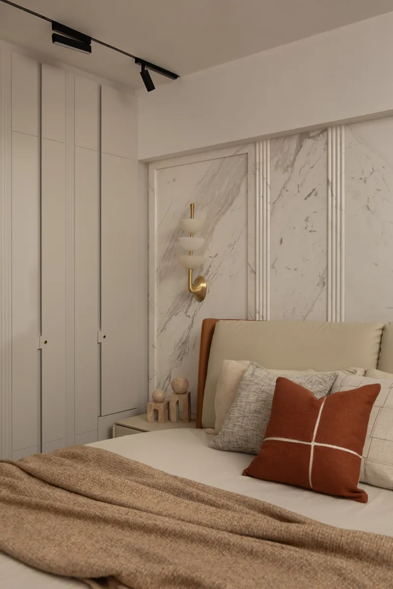 A bedroom with a book-matched marble feature wall and a brass-and-alabaster wall sconce.