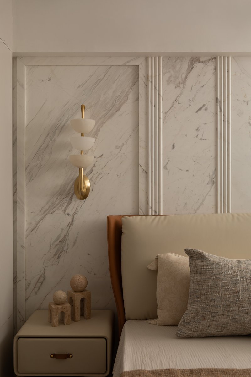 A bedside detail of the brass-and-alabaster sconce against the book-matched marble panel.