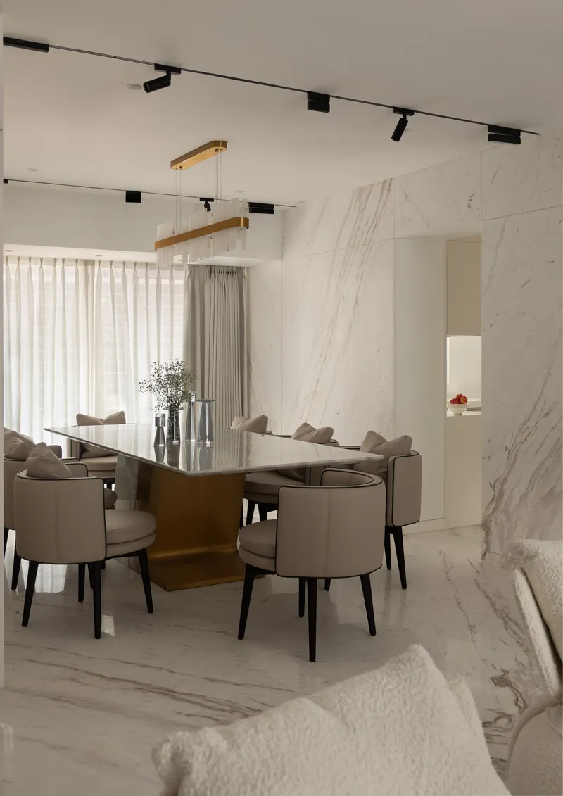 The dining table on its polished brass pedestal, against the continuous book-matched marble wall.