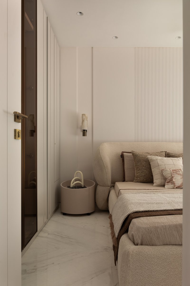A side view of the bouclé bed alongside a tinted brass-framed glass door and an alabaster wall sconce.
