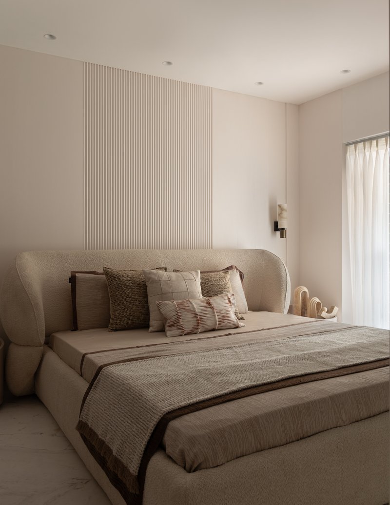 The second bedroom, with a curved bouclé headboard and a vertical fluted plaster panel.