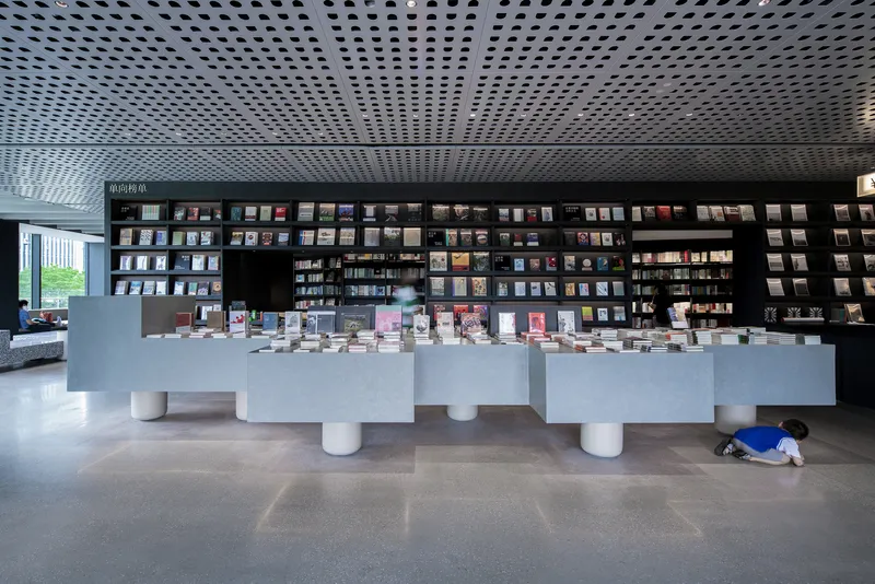 Bookstore interior with white display tables on cylindrical legs beneath a perforated metal ceiling