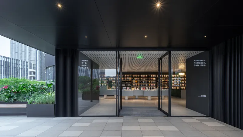 Entrance with pivoting glass doors flanked by planted beds and perforated metal ceiling soffit
