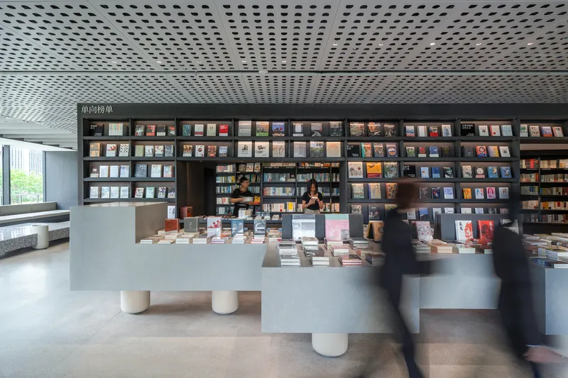 Bookstore service counter with terrazzo base and floor-to-ceiling display shelving under perforated ceiling