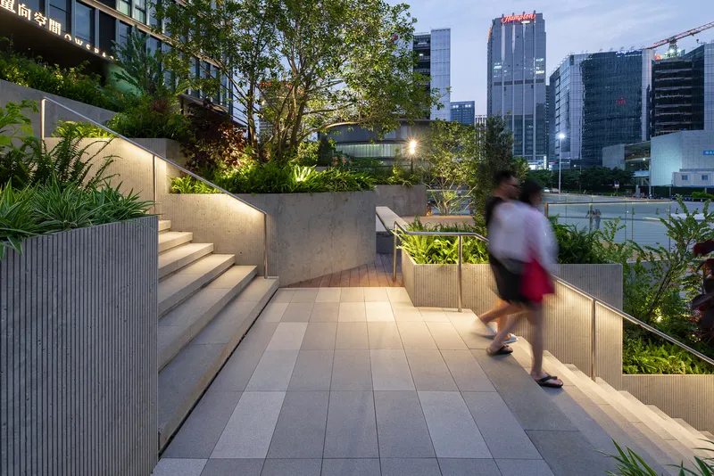 Terraced paved pathway with integrated planters and a person in motion at dusk