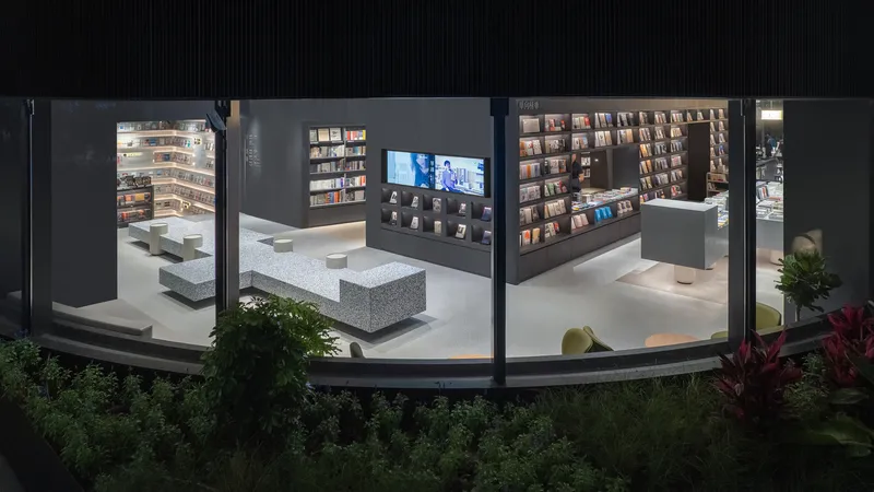 Storefront window framing an interior bookstore with terrazzo seating cubes and wall shelving at night