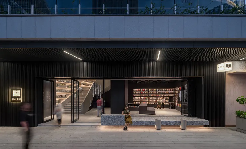 Storefront entry with black corrugated metal facade and glazed openings revealing bookshelves at dusk