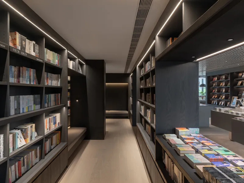 Narrow aisle flanked by tall dark timber bookshelves with recessed LED lighting strips