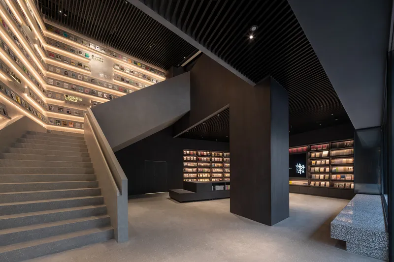 Open atrium with illuminated bookshelf walls and terrazzo stairs ascending toward slatted ceiling